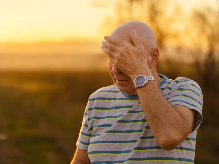 Older man wiping forehead during outdoor walk on hot day