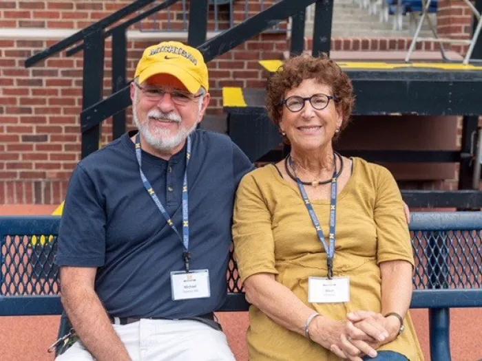 Smiling photo of Fishman and DiPietro seated together on an outdoor bench.