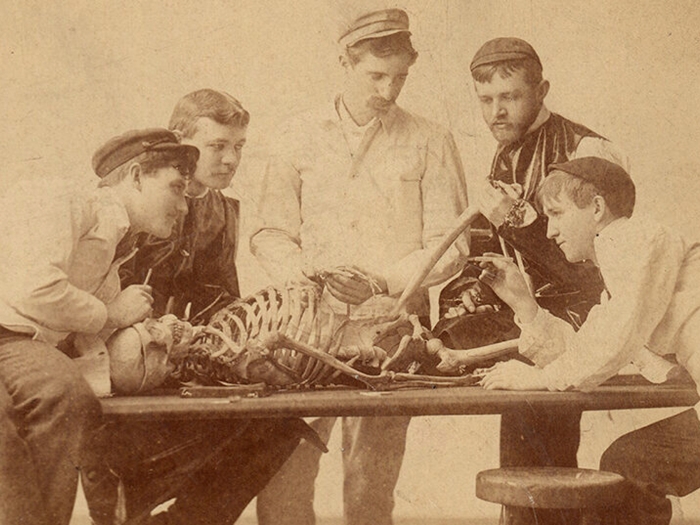 old photo of men sitting around skeleton on table talking