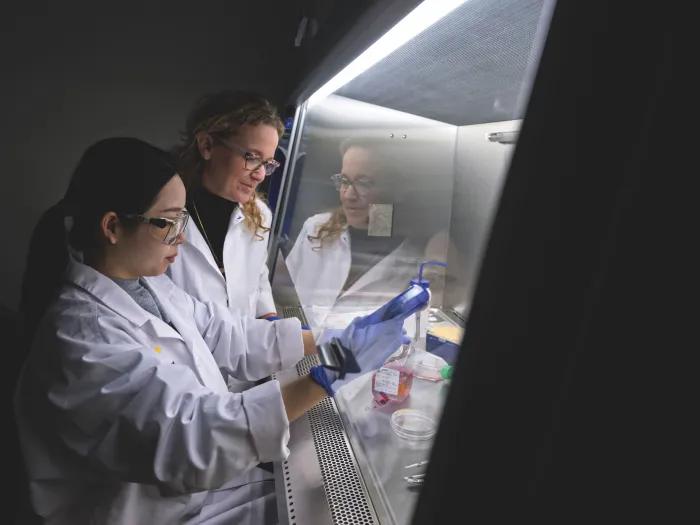 Michelle Hastings (right) and a student are working in the lab. They are wearing white lab coats and the student is holding lab equipment.