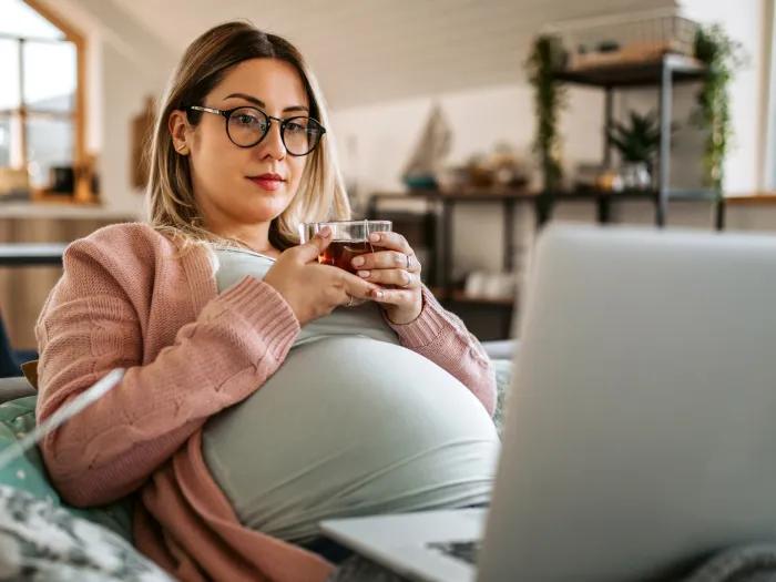 woman pregnant sitting holding tea and glasses on brown hair