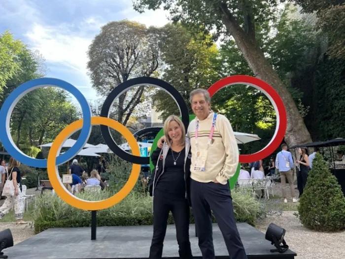 Photo of the Gewertzes standing together in a park-like area in front of a large display of the Olympic rings.