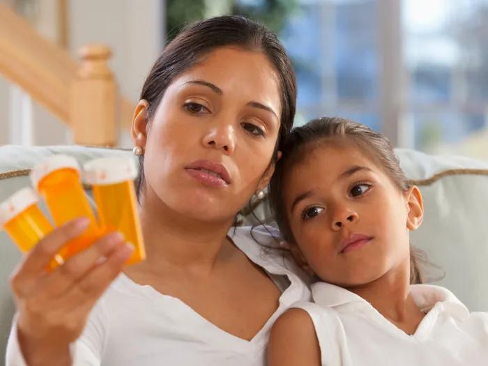 woman looking at orange empty pill bottles with daughter on couch