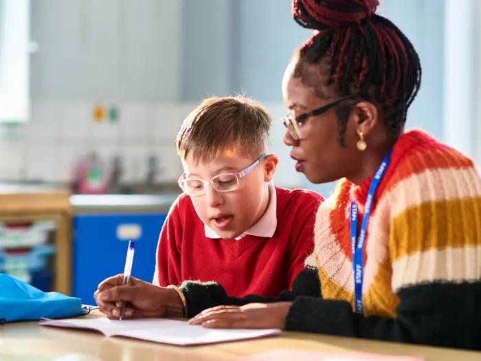kid sitting with woman doing work at desk in classroom