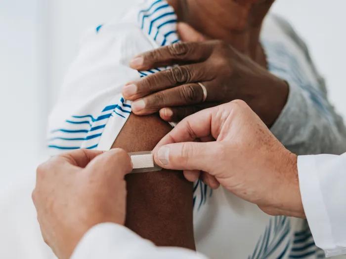 person pulling up sleeve getting bandaid from person with white coat sleeves all close up and whiter background