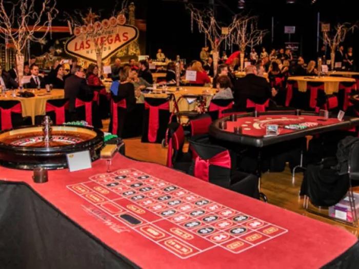 View of Casino Royale event with a roulette table in the foreground and additional casino tables surrounded by guests in the background.