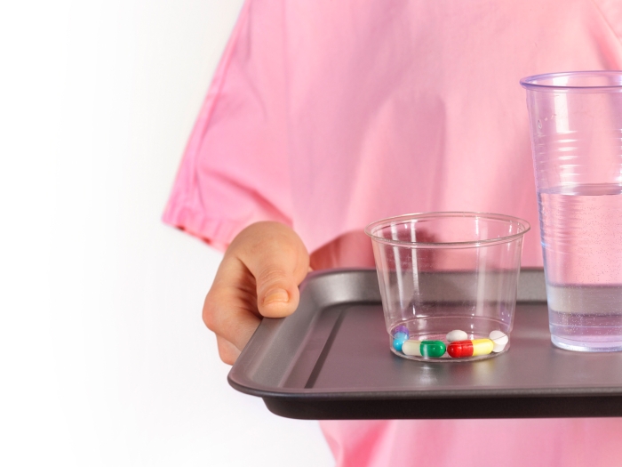 pills in a cup water in a cup both on a tray with a patient in pink gown