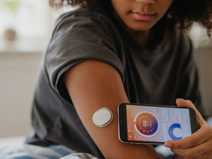 teen girl in t-shirt checking device on arm linked to phone which she holds up to her arm 