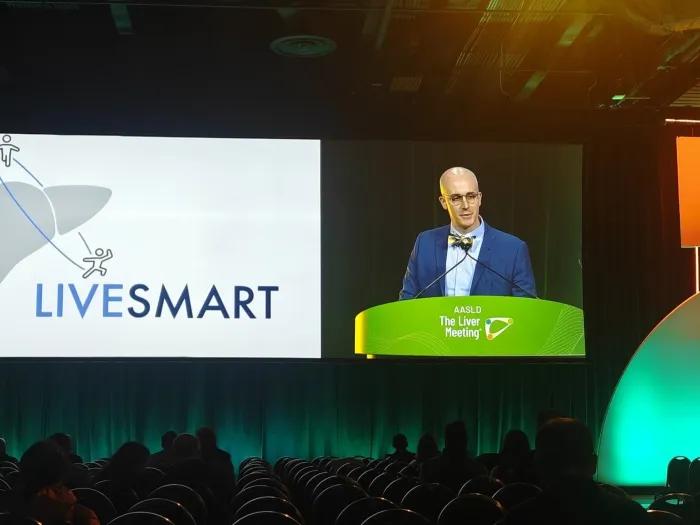 man presenting at conference with glasses dark room screen