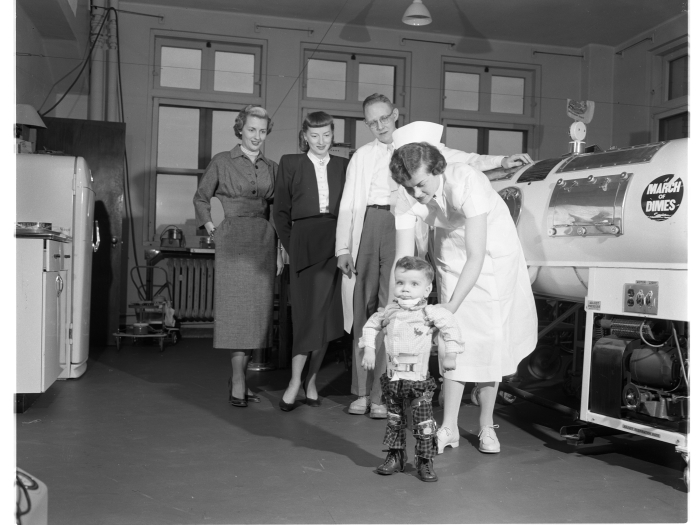 A toddler in braces near an iron lung in U-M polio unit 1950s