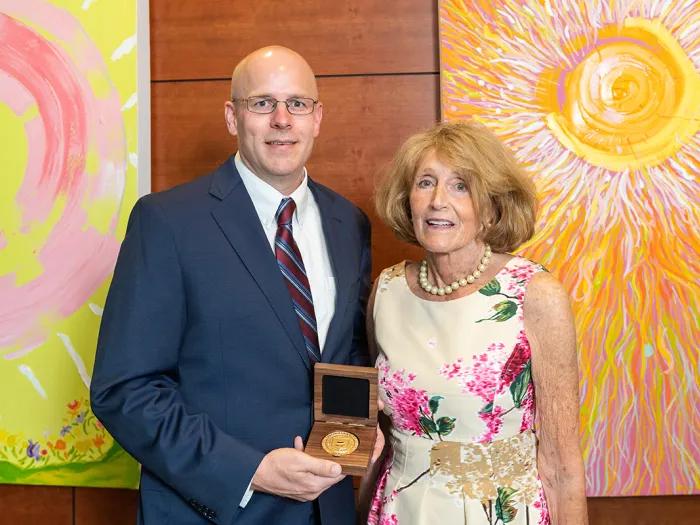 Paul Pfeiffer, M.D., and Susan Brown standing together and smiling at Pfeiffer's professorship inauguration. They are both wearing dress clothes and Pfeiffer is displaying his gold professorship medal in a small wooden case.