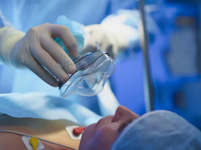 woman prepped for surgery with mask going over mouth in surgical setting blue scrubs on all pictured and white gloves 