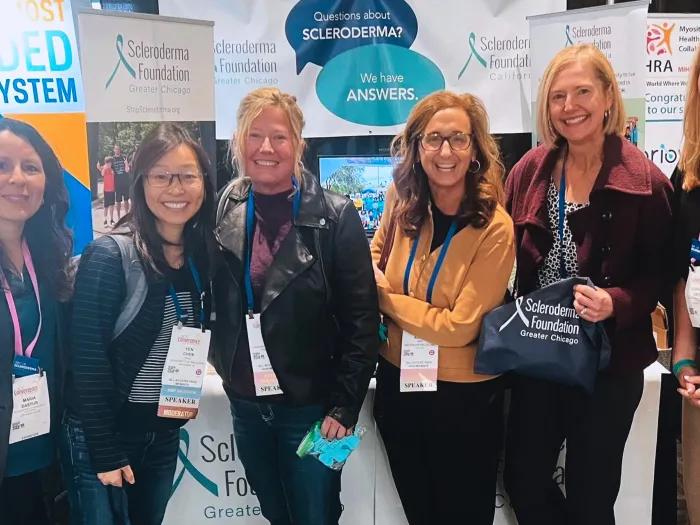 six women standing together smiling in front of posters