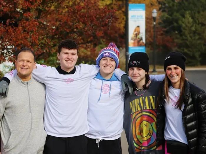 Marc, Brody, Max, Caroline, and Alyssa Tushman standing with their arms over each others' shoulders and smiling toward the camera. They're wearing cold weather gear and fall foliage is visible behind them.