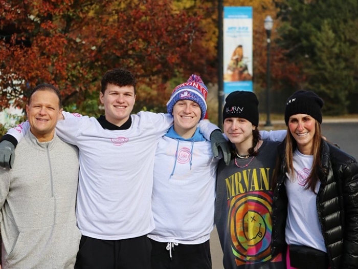 Marc, Brody, Max, Caroline, and Alyssa Tushman standing with their arms over each others' shoulders and smiling toward the camera. They're wearing cold weather gear and fall foliage is visible behind them.