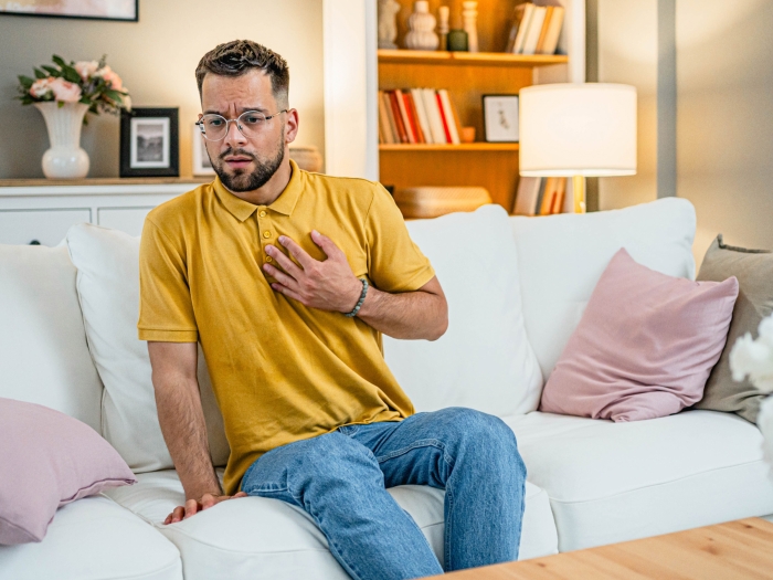 man holding chest with yellow shirt sitting on white couch concerned