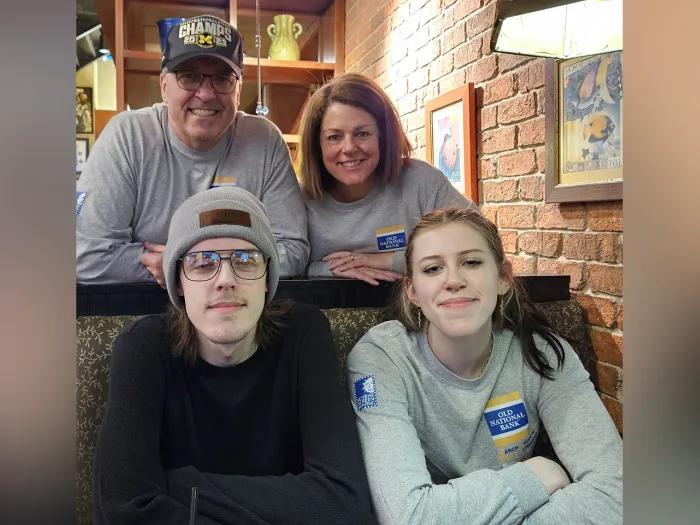 The Hepner family together in what appears to be their living room. The two young adults are seated on a couch and the two parents lean in behind them. All are smiling.
