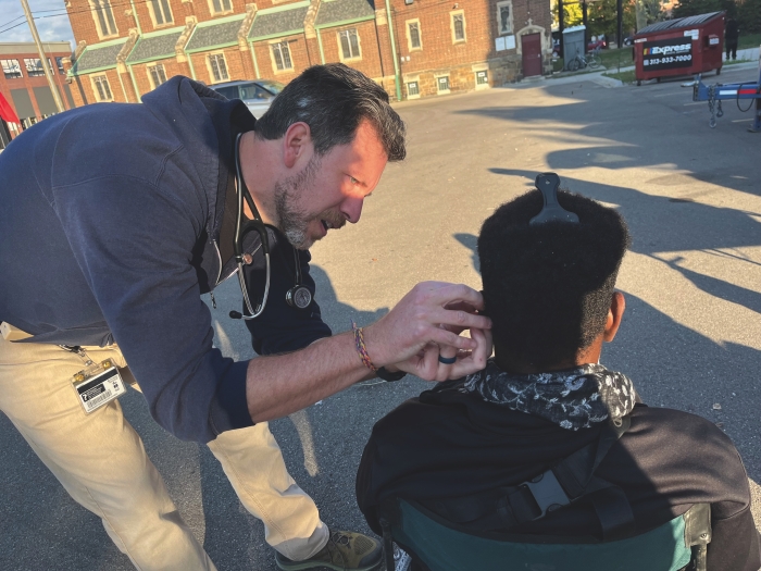 Neil Nixdorff is standing next to a man who is seated. Nixdorff is applying acupuncture to the man's ear.