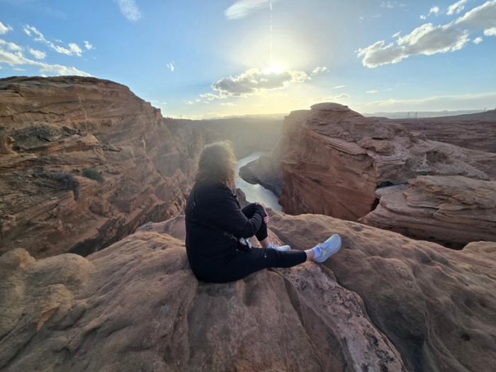 Woman sits with back facing to camera looking out over a sunny canyon 