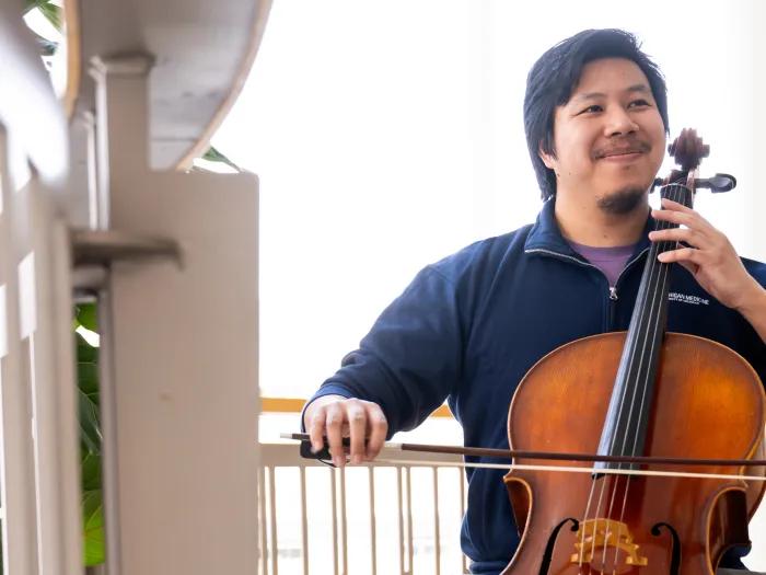 Med student Curtis Kuo plays the cello. He's smiling slightly and looking off in the distance.