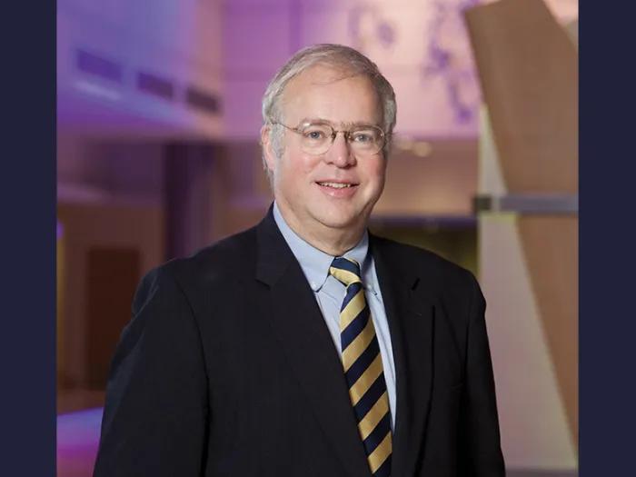 Portrait of Timothy Johnson wearing a suit and tie and standing in the lobby of a University of Michigan hospital