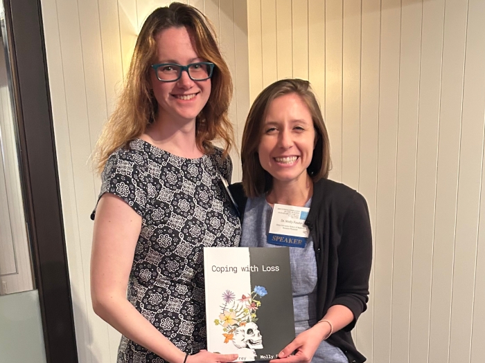 Two women stand posing with a book held between them.