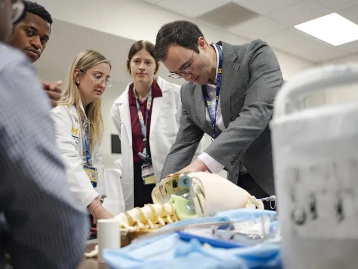 Five medical students stand around a table and work with an anatomical model torso.