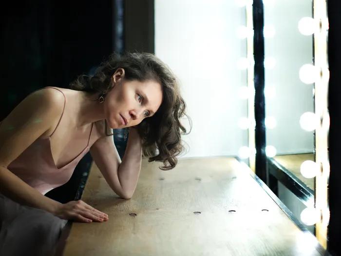A woman who appears sad or thoughtful is seated in front of a mirror.