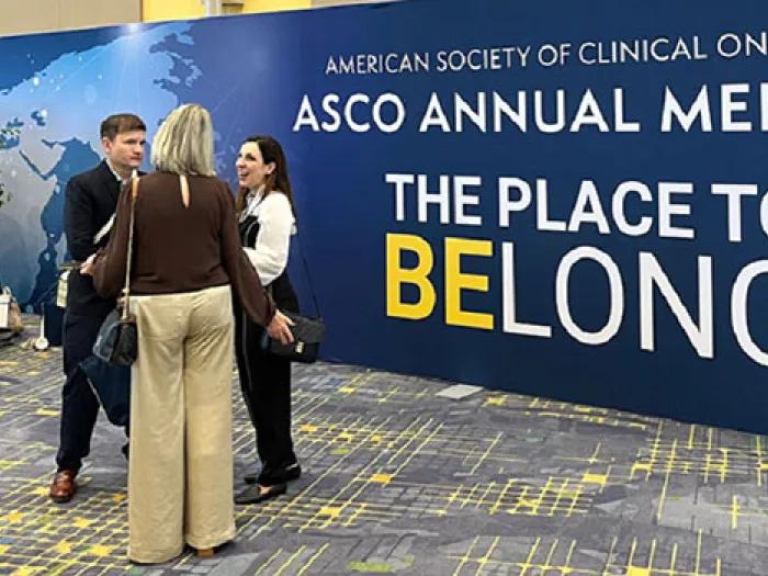 Men and women stand in groups chatting in front of the ASCO 2025 logo sign