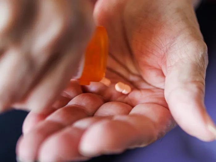 A pill bottle is open and pills are placed onto a hand