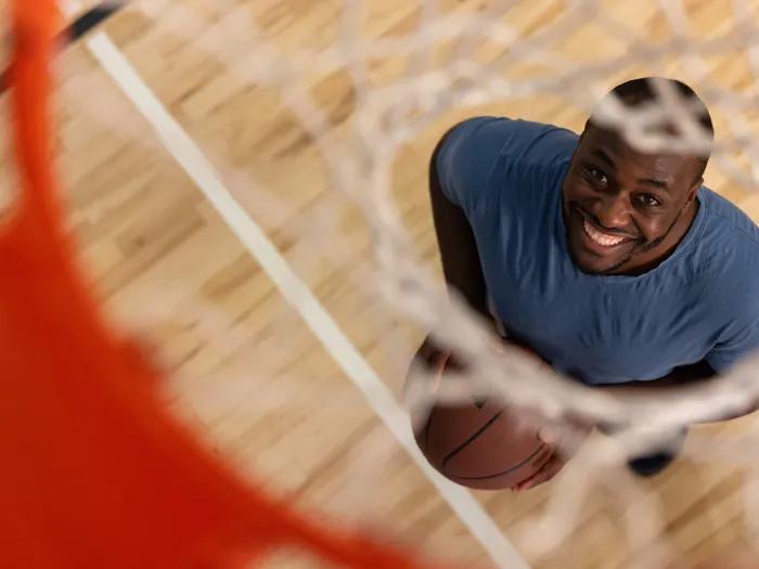 Man stands under a basketball hoop, smiling through the net