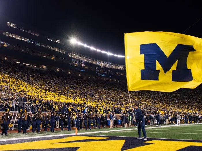 Man holding UM flag on UM football field, athletics