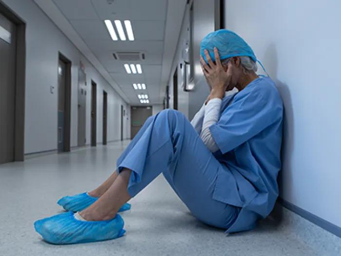 female surgeon on ground upset hands to face in scrubs and scrub shoes