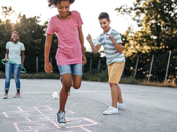 children playing hopscotch outside with no masks and trees on pavement