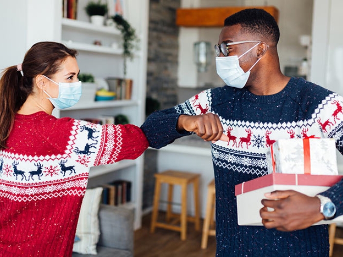 two people bumping elbows in masks in holiday sweaters red and navy