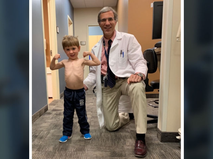 Doctor kneeling in clinic next to child flexing muscles