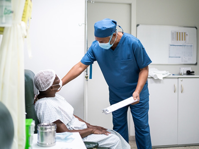 doctor in mask with clipboard reaching down to patients shoulder sitting with mask on
