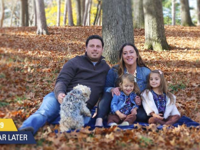family of 4 with dog sitting against tree on fall leaves