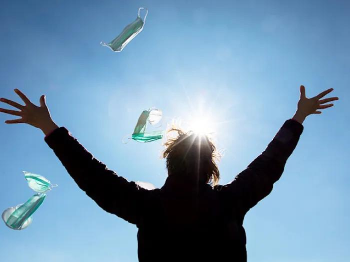 person throwing masks into the sky with sun