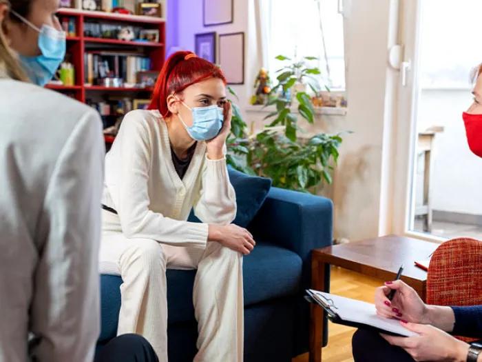 girl talking to counselor with red hair on couch with parent there too in masks