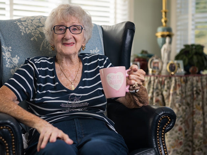 grandmother smiling with pink mug in hand in chair sitting