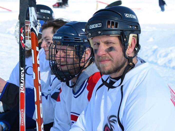 Hockey players sitting on bench with sticks snow in background