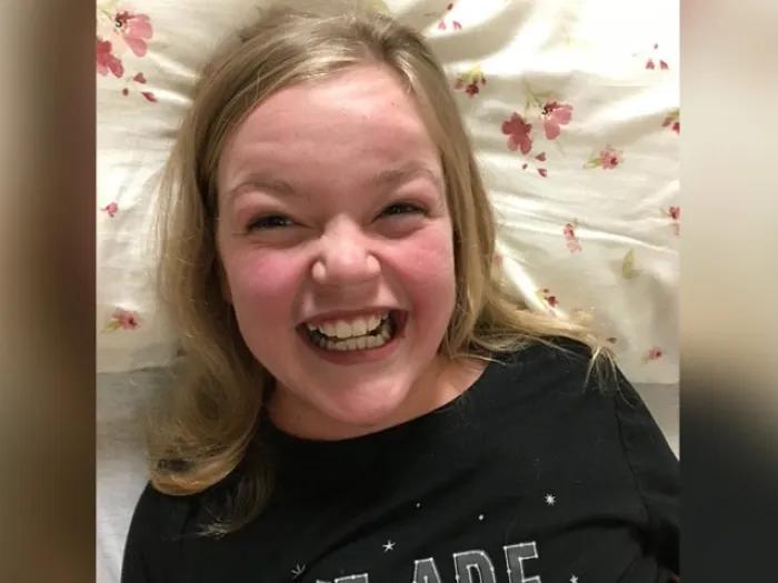 teen girl smiling in navy shirt with blonde hair laying on pillow