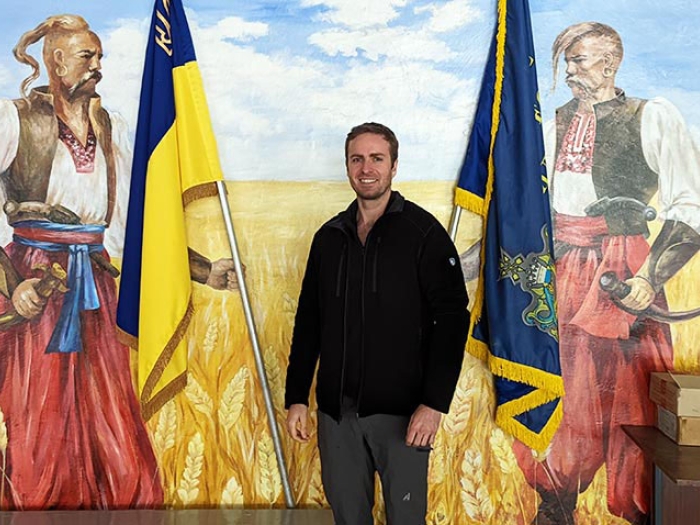 Man smiling with mural Ukraine flags in background.