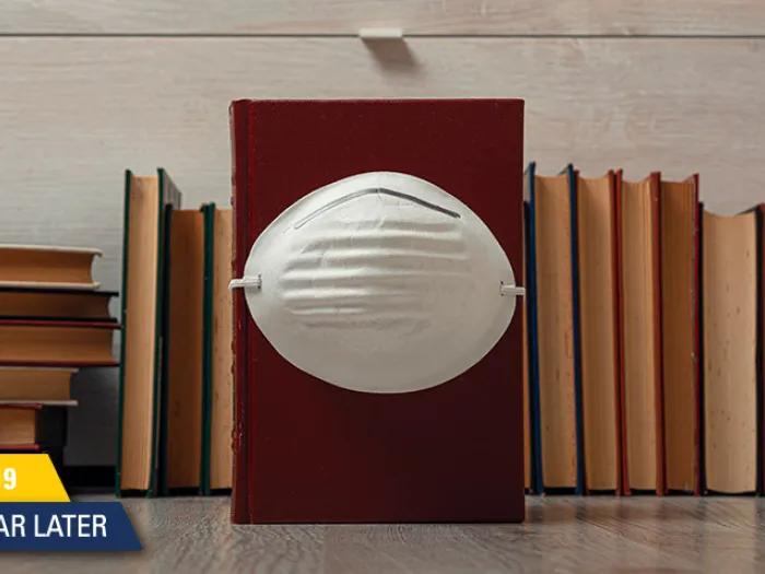 mask on brown books with covid anniversary stamp on bottom left in yellow and blue