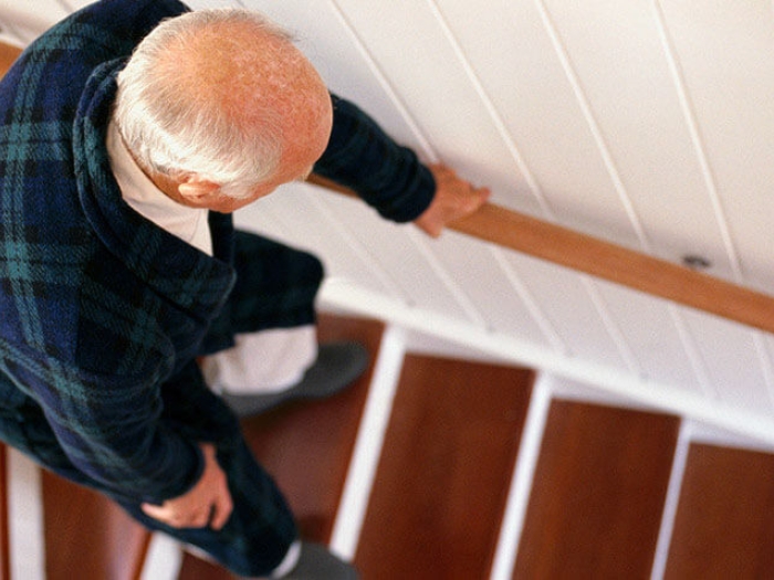 Senior man bending while walking down wooden stairs holding onto rail