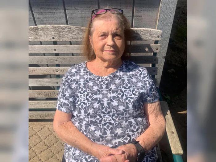 senior woman sitting smiling on bench in blue floral shirt