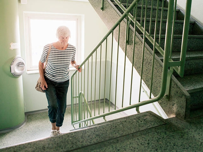 senior woman climbs stairs and holds railing