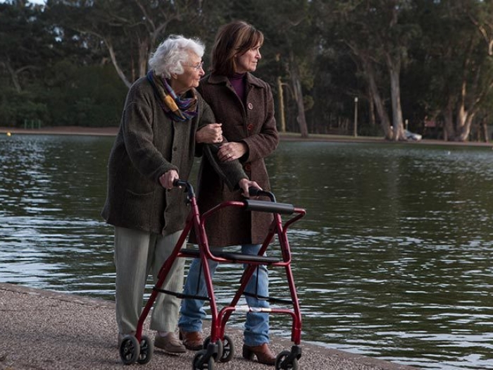 senior woman walking with walker with woman by pond