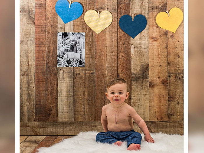 Baby smiling while sitting on fuzzy white rug, hearts and picture on wood background